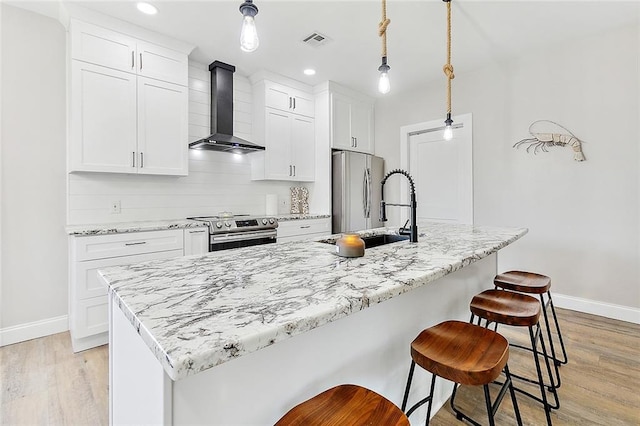 kitchen featuring appliances with stainless steel finishes, a kitchen bar, wall chimney range hood, and an island with sink