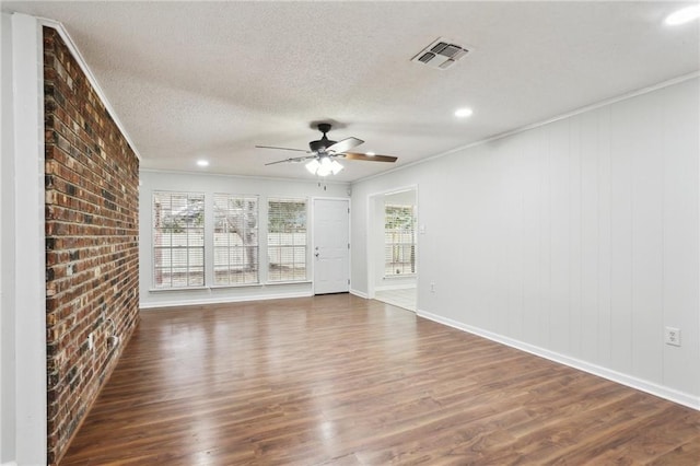 unfurnished living room with ceiling fan, a textured ceiling, dark hardwood / wood-style floors, crown molding, and brick wall