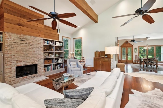 living room featuring high vaulted ceiling, hardwood / wood-style floors, a brick fireplace, ceiling fan, and beam ceiling