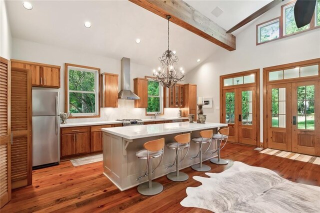 kitchen featuring a notable chandelier, appliances with stainless steel finishes, a center island, dark wood-type flooring, and wall chimney range hood