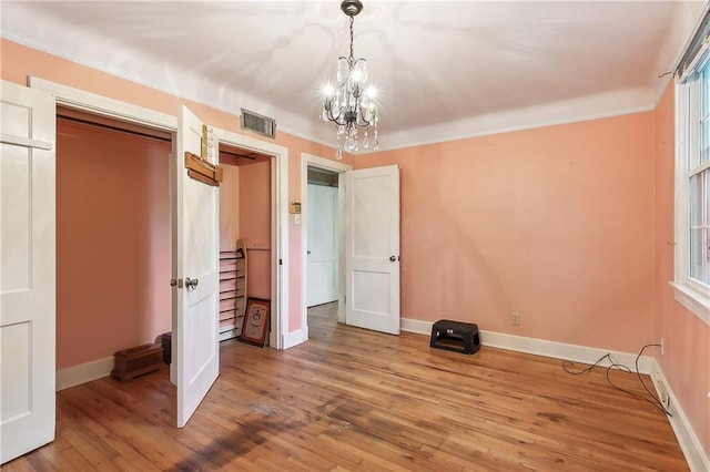 unfurnished bedroom featuring hardwood / wood-style flooring, a chandelier, a closet, and ornamental molding