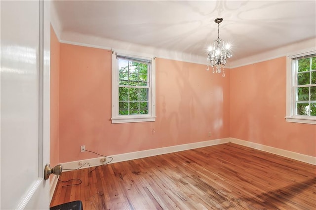 unfurnished room with wood-type flooring, a healthy amount of sunlight, an inviting chandelier, and crown molding