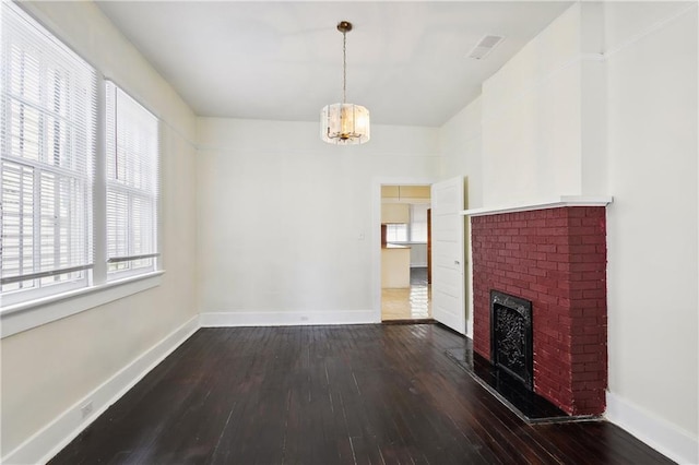 unfurnished living room featuring dark wood-type flooring, a notable chandelier, and a brick fireplace