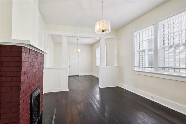 unfurnished living room featuring a fireplace, heating unit, a chandelier, ornate columns, and dark hardwood / wood-style floors