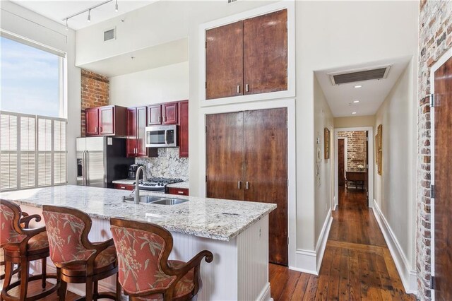 kitchen featuring dark hardwood / wood-style floors, a kitchen island with sink, stainless steel appliances, rail lighting, and light stone counters