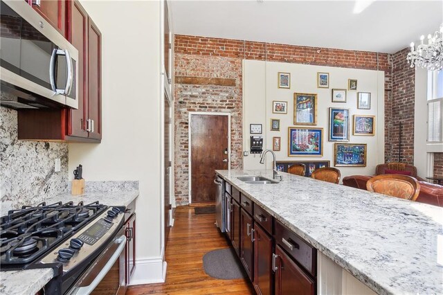 kitchen featuring brick wall, light stone countertops, appliances with stainless steel finishes, sink, and light wood-type flooring