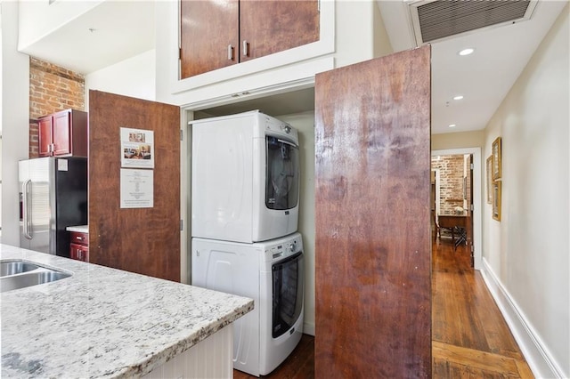 kitchen with dark hardwood / wood-style flooring, stainless steel refrigerator, brick wall, and stacked washer and clothes dryer