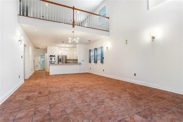 unfurnished living room with an inviting chandelier, tile patterned flooring, and a towering ceiling