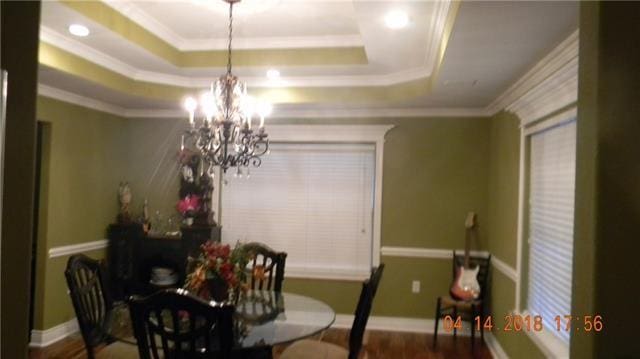 dining space with a tray ceiling, an inviting chandelier, wood-type flooring, and ornamental molding