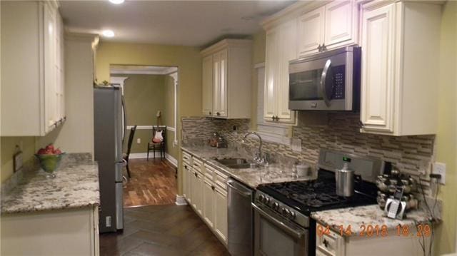 kitchen featuring backsplash, light stone countertops, appliances with stainless steel finishes, white cabinetry, and sink