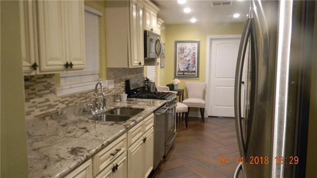 kitchen with cream cabinets, light stone counters, stainless steel appliances, sink, and tasteful backsplash