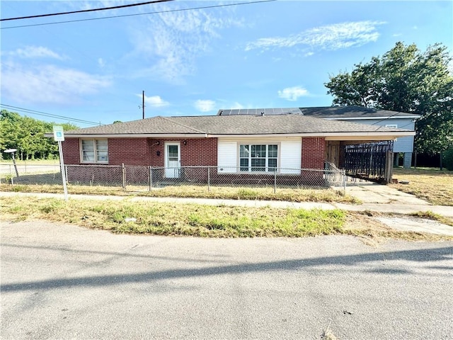 single story home featuring a fenced front yard, an attached carport, solar panels, and brick siding