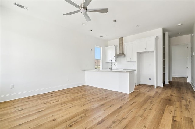 kitchen featuring ceiling fan, decorative light fixtures, wall chimney exhaust hood, white cabinetry, and light hardwood / wood-style floors