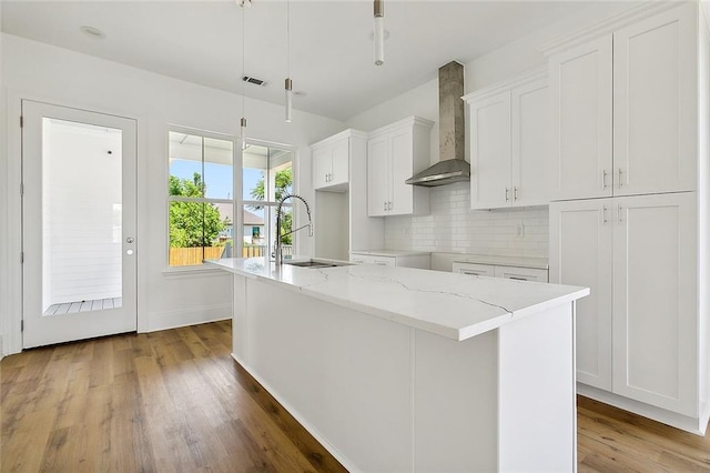 kitchen featuring wall chimney exhaust hood, white cabinetry, sink, and an island with sink