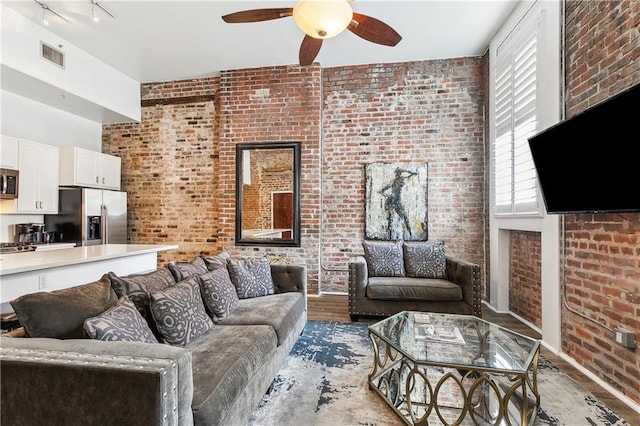 living room featuring rail lighting, hardwood / wood-style flooring, ceiling fan, and brick wall