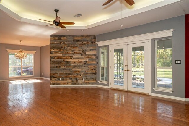 unfurnished living room featuring french doors, hardwood / wood-style floors, a tray ceiling, and ceiling fan with notable chandelier