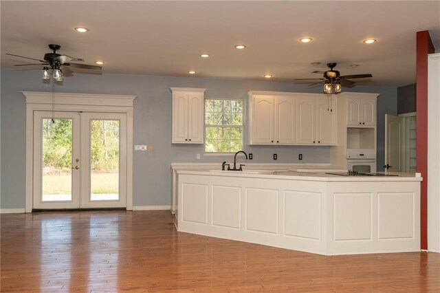 kitchen with black electric stovetop, oven, kitchen peninsula, and white cabinets