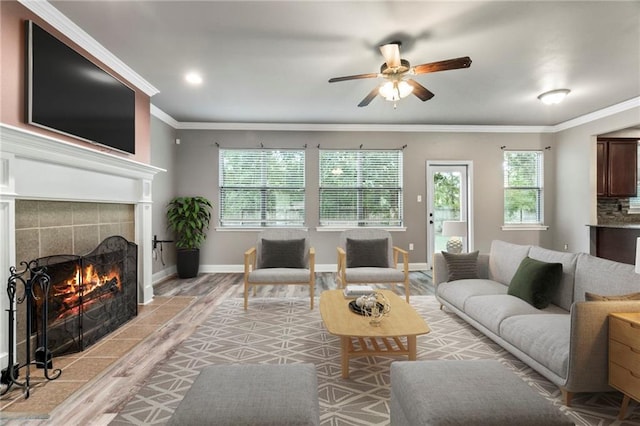 living room featuring ceiling fan, crown molding, a tile fireplace, and light hardwood / wood-style flooring