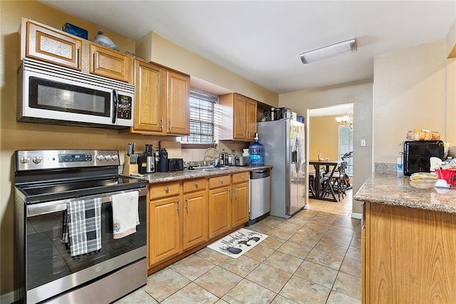 kitchen with sink, an inviting chandelier, appliances with stainless steel finishes, light tile patterned floors, and light stone countertops