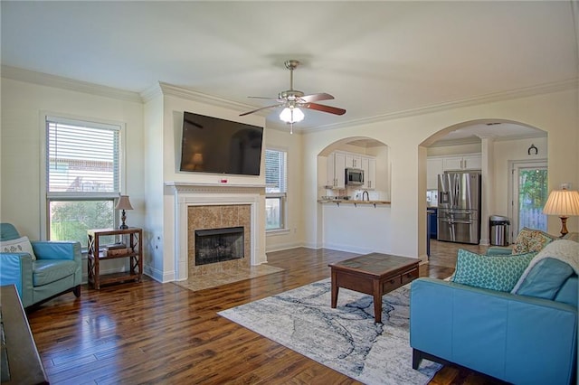 living room featuring dark wood-type flooring, ceiling fan, ornamental molding, and a fireplace