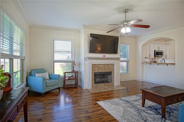 living room featuring a tile fireplace, ornamental molding, dark hardwood / wood-style floors, and ceiling fan