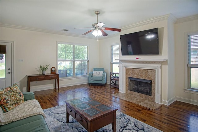 living room with dark wood-type flooring, ceiling fan, ornamental molding, and a tiled fireplace