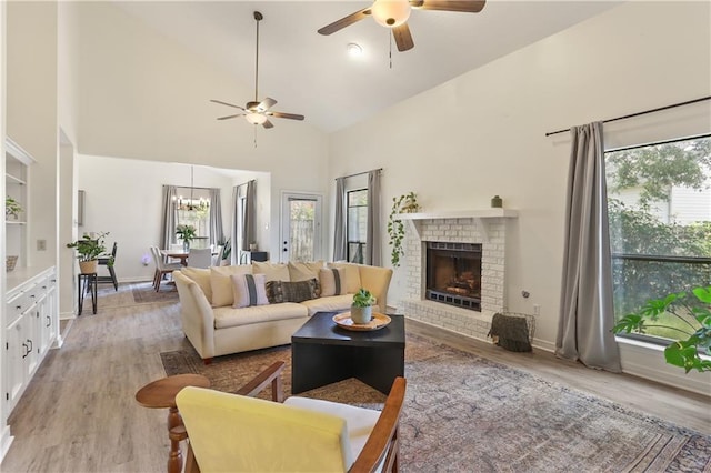 living room with light hardwood / wood-style floors, ceiling fan with notable chandelier, high vaulted ceiling, and a fireplace