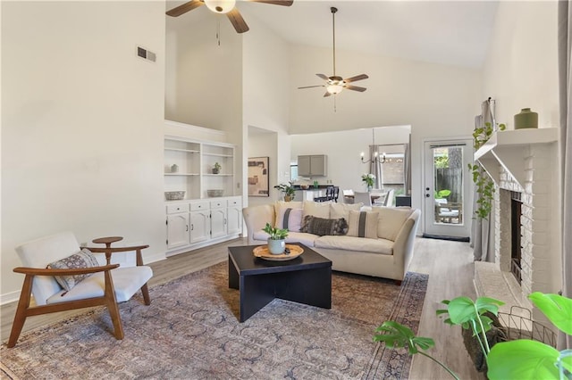 living room featuring high vaulted ceiling, ceiling fan, a brick fireplace, and hardwood / wood-style flooring