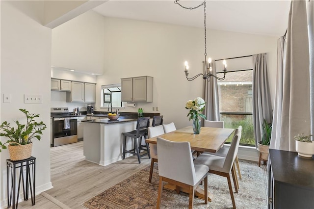 dining area with light hardwood / wood-style flooring, high vaulted ceiling, an inviting chandelier, and a healthy amount of sunlight