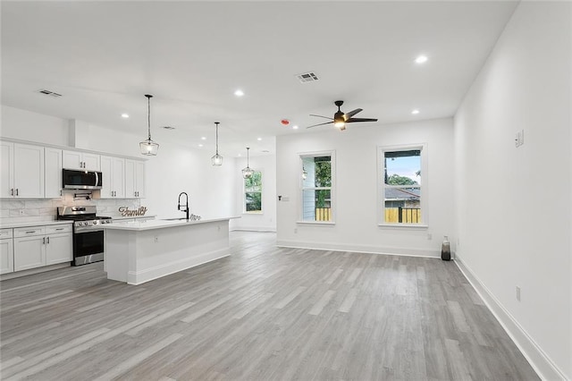 kitchen with white cabinets, light hardwood / wood-style flooring, appliances with stainless steel finishes, ceiling fan, and a kitchen island with sink