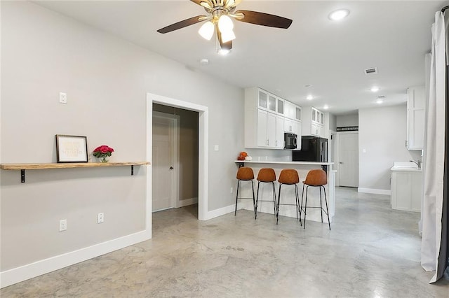 kitchen with white cabinetry, black appliances, a breakfast bar area, kitchen peninsula, and ceiling fan