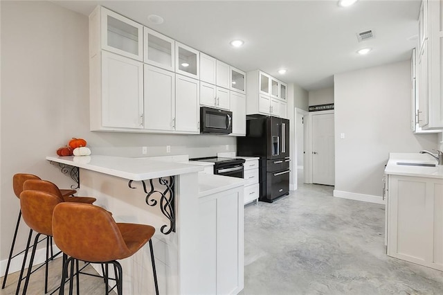 kitchen with black appliances, a breakfast bar, sink, and white cabinets