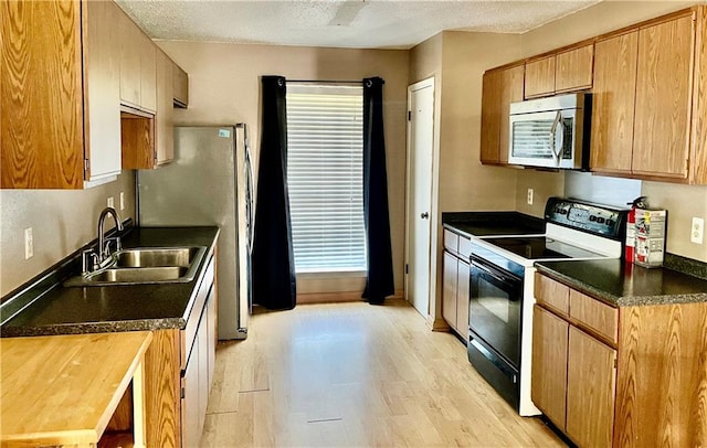 kitchen with a textured ceiling, sink, appliances with stainless steel finishes, and light hardwood / wood-style floors