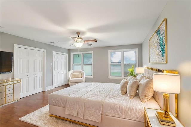 bedroom with hardwood / wood-style flooring, ceiling fan, and two closets