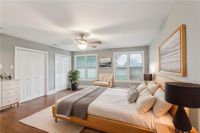 bedroom with dark hardwood / wood-style flooring, two closets, and ceiling fan