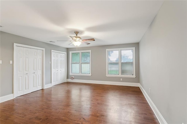 unfurnished bedroom with ceiling fan, dark hardwood / wood-style floors, and multiple closets