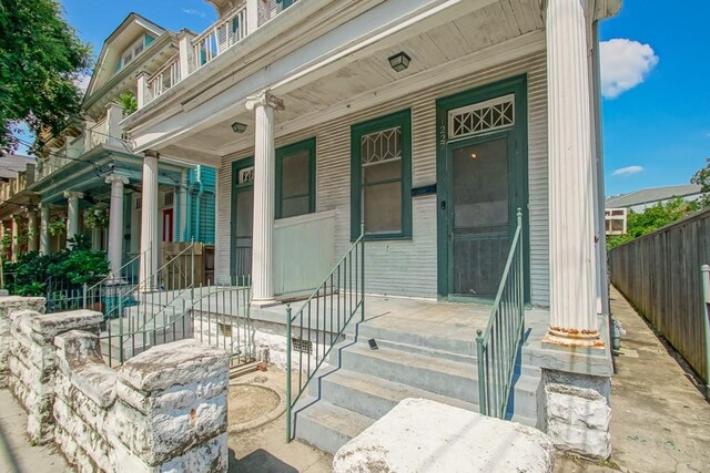 doorway to property with covered porch and fence