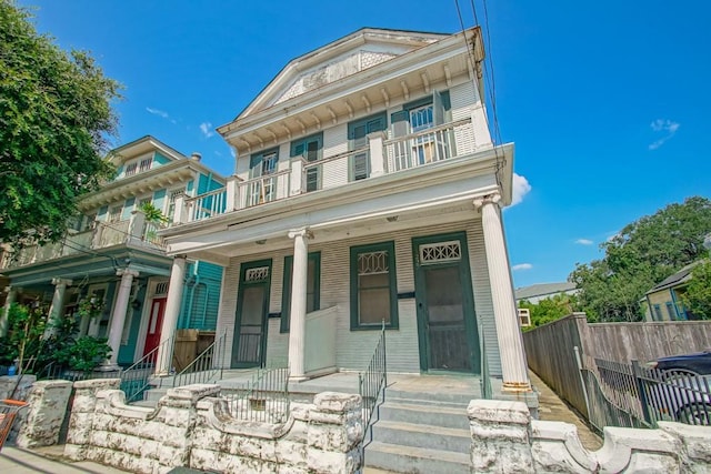 greek revival house featuring covered porch, fence, and a balcony