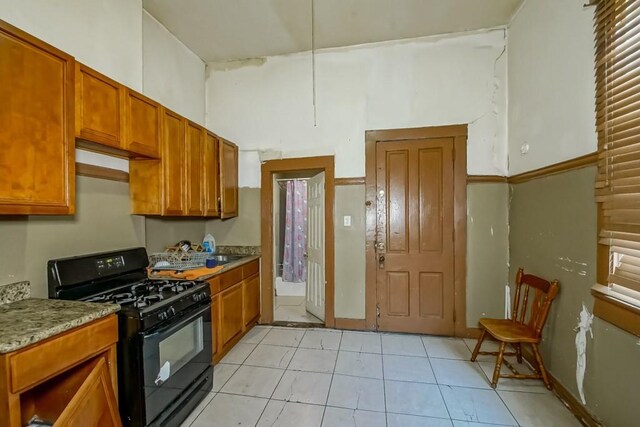 122729 Carondelet St, New Orleans, LA 70130 - kitchen with brown cabinetry, light tile patterned flooring, black gas range oven, and a towering ceiling