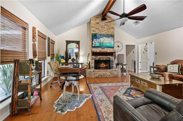 living room with a textured ceiling, a fireplace, light hardwood / wood-style floors, ceiling fan, and vaulted ceiling with beams