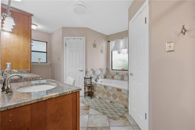 bathroom featuring plenty of natural light, tiled bath, and vanity