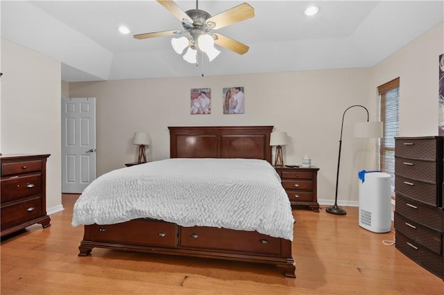 bedroom with light wood-type flooring, a tray ceiling, and ceiling fan