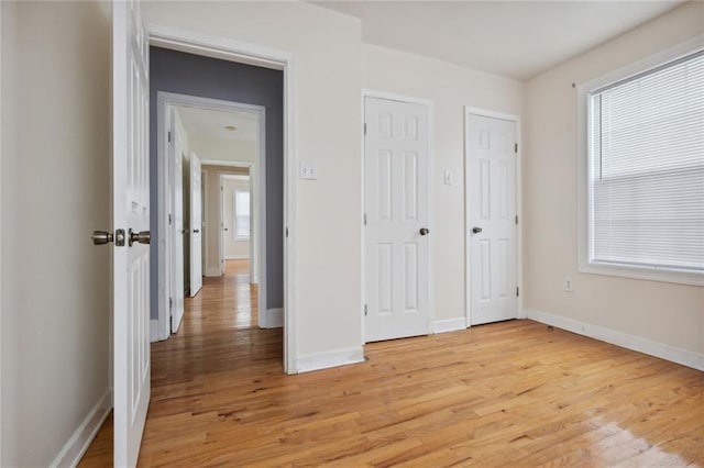 unfurnished bedroom featuring light wood-type flooring, multiple windows, and two closets