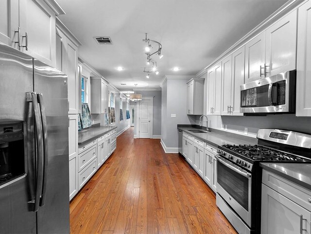 kitchen featuring sink, stainless steel appliances, crown molding, white cabinets, and light wood-type flooring