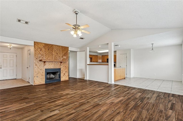 unfurnished living room featuring ceiling fan, vaulted ceiling, a tile fireplace, and hardwood / wood-style flooring