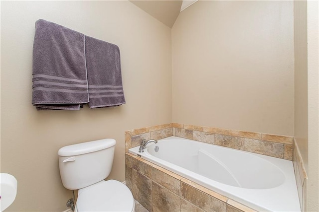 bathroom featuring lofted ceiling, tiled tub, and toilet