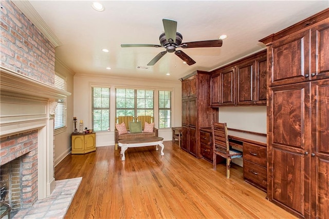 office area with built in desk, ceiling fan, a fireplace, and light hardwood / wood-style floors