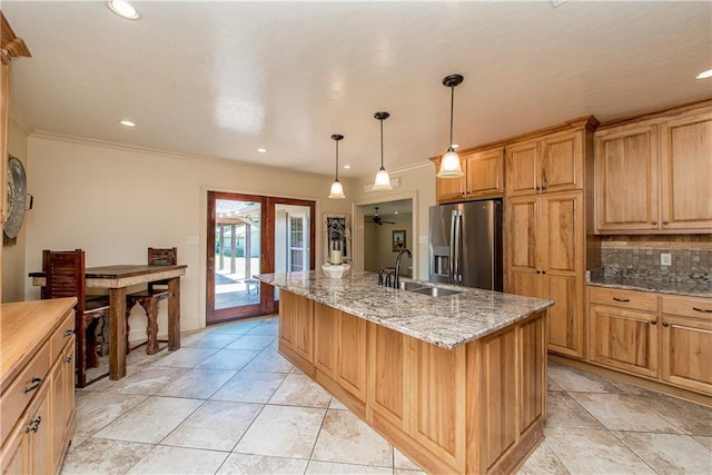 kitchen featuring an island with sink, a sink, stainless steel fridge, crown molding, and tasteful backsplash