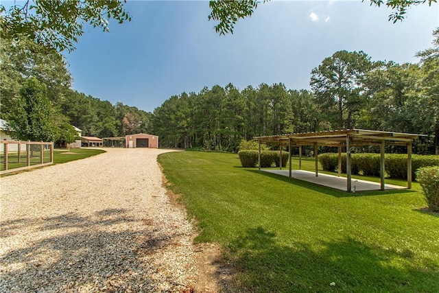 view of home's community featuring a view of trees, a garage, a yard, an outbuilding, and a patio