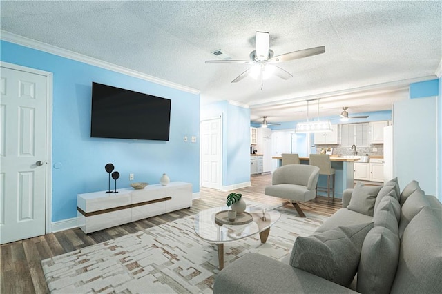 living room with ceiling fan, ornamental molding, light hardwood / wood-style flooring, and a textured ceiling